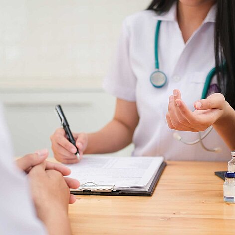 Heller Arbeitsplatz mit Fensterbank zum Sitzen, Kissen, Laptop auf kleinem Tisch und großer Zimmerpflanze neben dem Fenster. An der Wand Fenster mit Sicht auf Stadt und bunte Notizzettel am Rand. Atmosphäre wirkt ruhig und einladend.